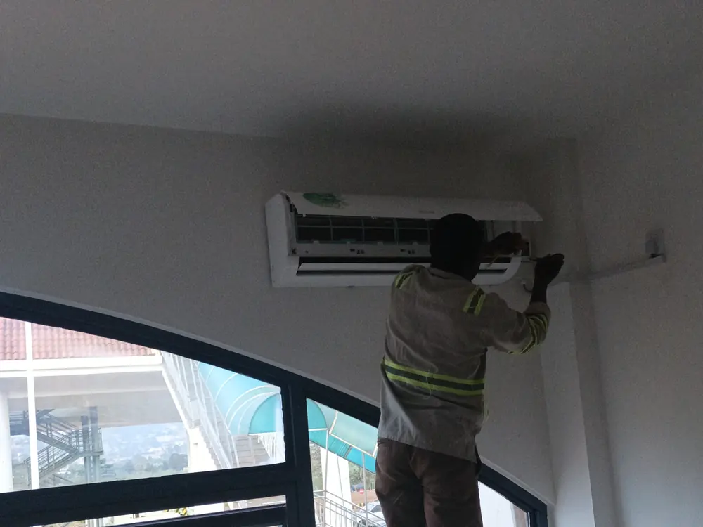 Technician on a ladder servicing a wall-mounted air conditioner